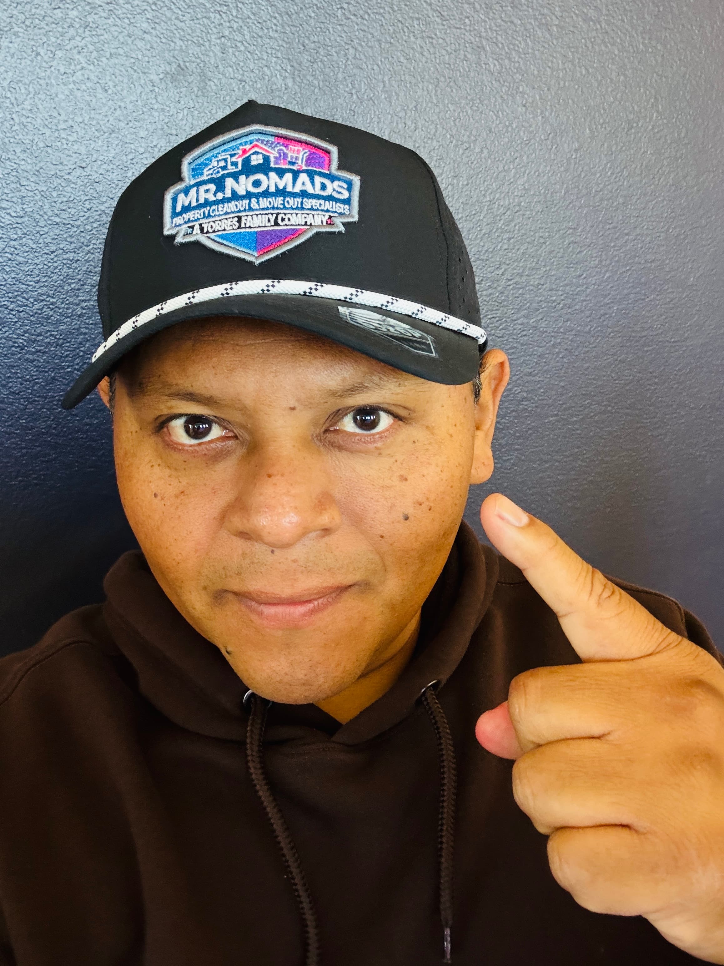 Man wearing a brown hoodie and a Mr. Nomads branded cap pointing his finger.